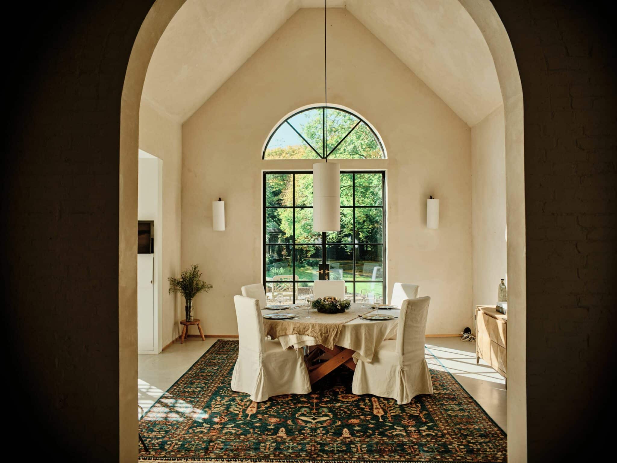 A bright dining room with a Persian rug from London Persian Rug Company under the table, arched window, and elegant décor.